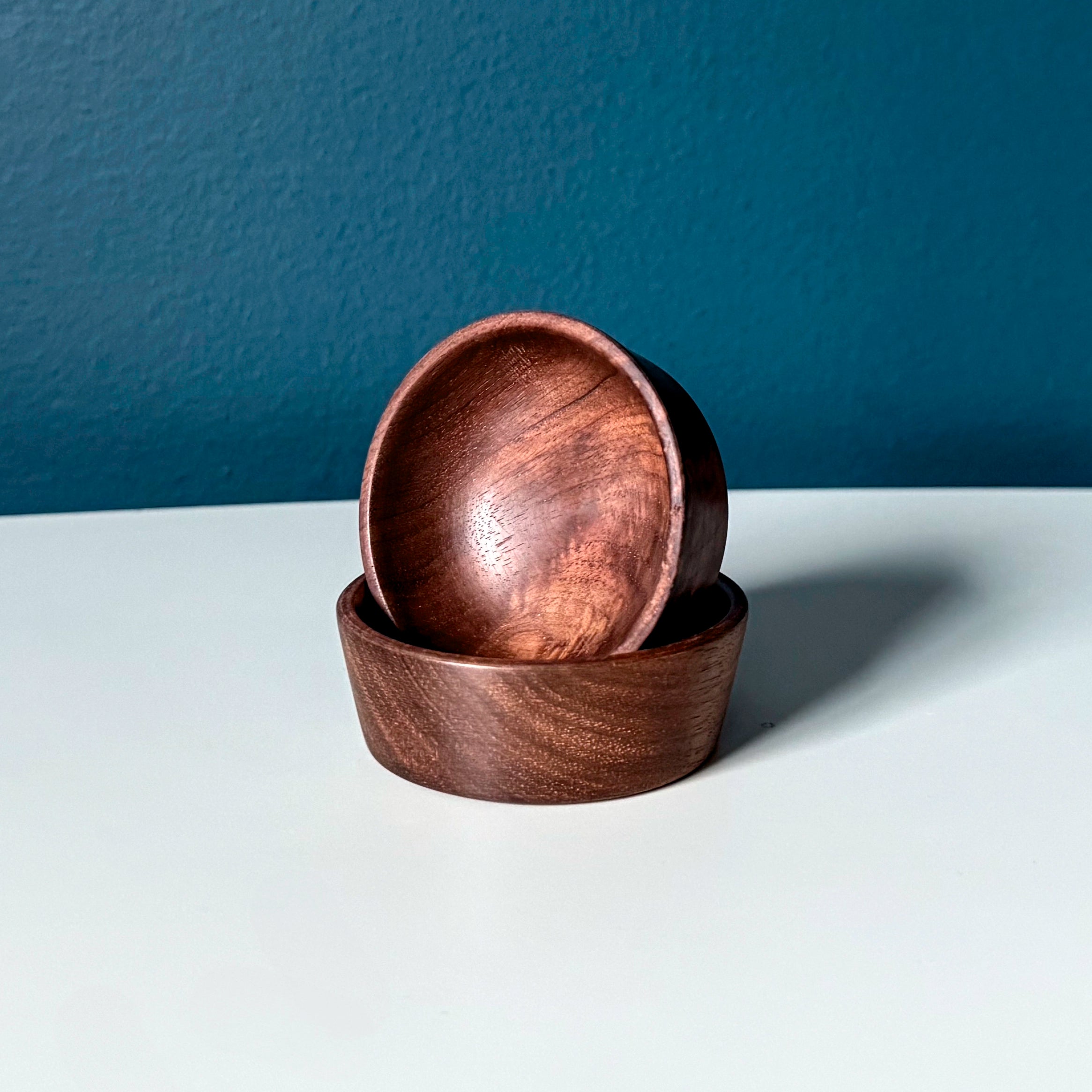 Two wooden bowls stacked on a white surface with a dark blue background