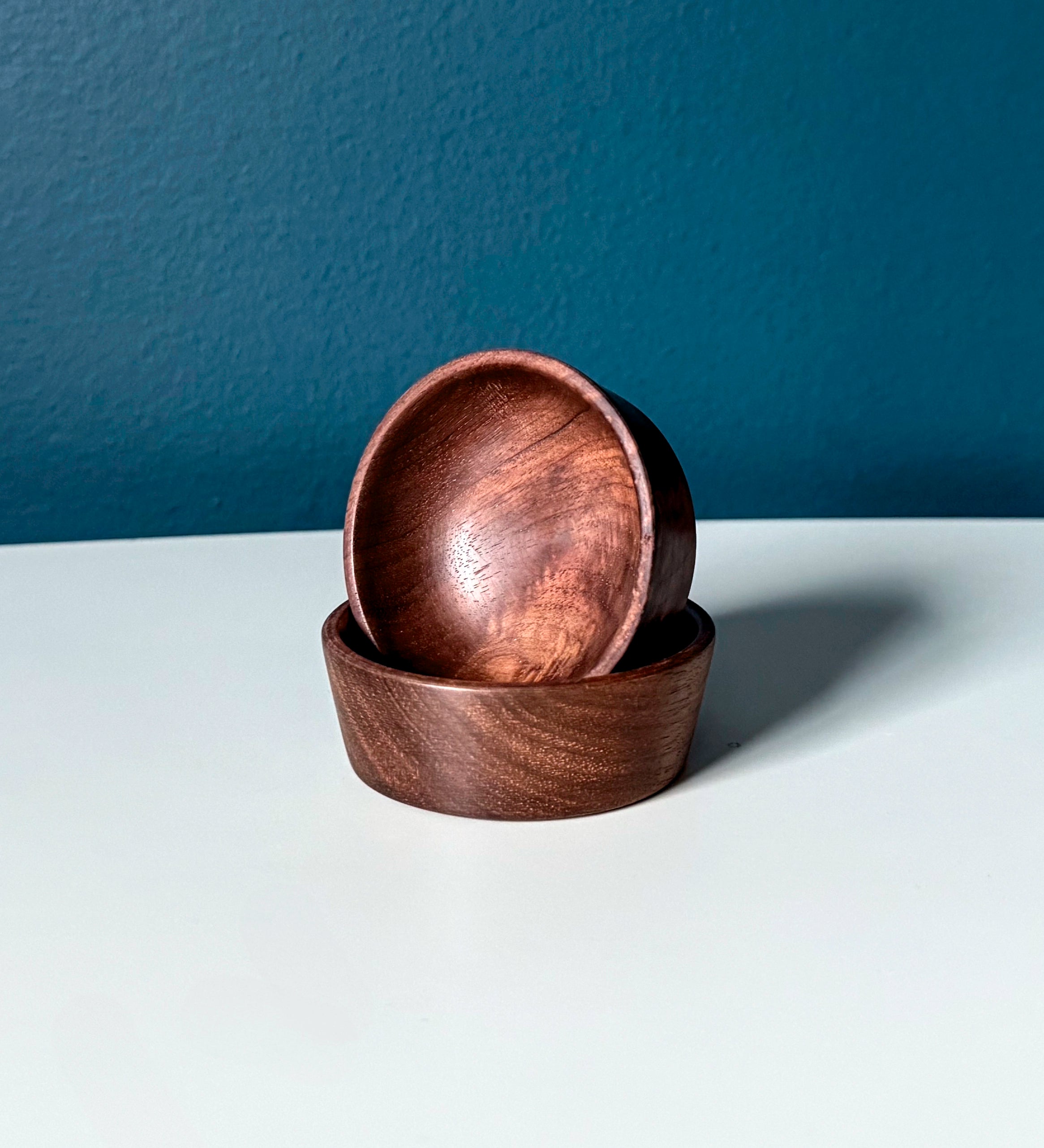 Two wooden bowls stacked on a white surface with a dark blue background
