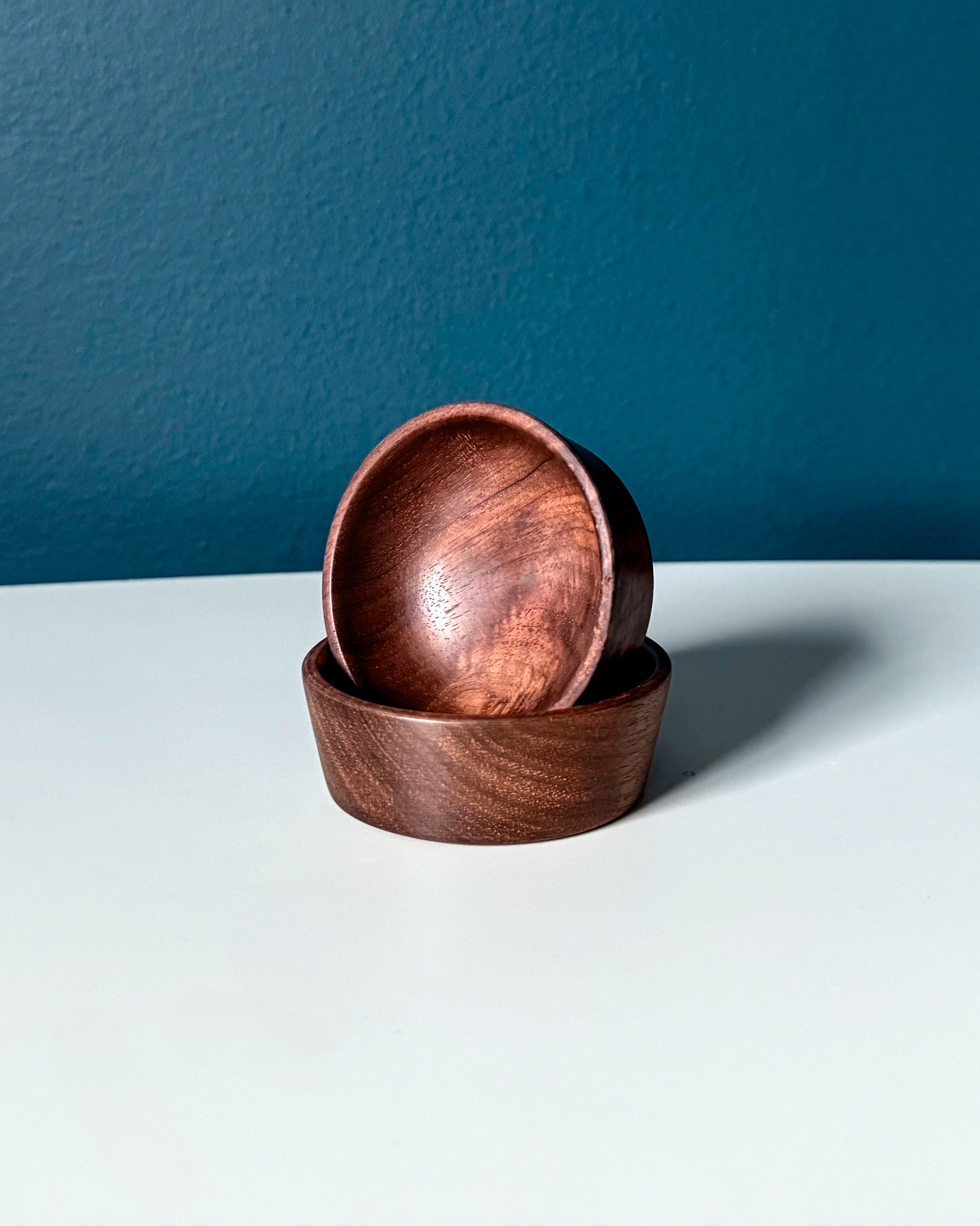 Two wooden bowls stacked on a white surface with a dark blue background