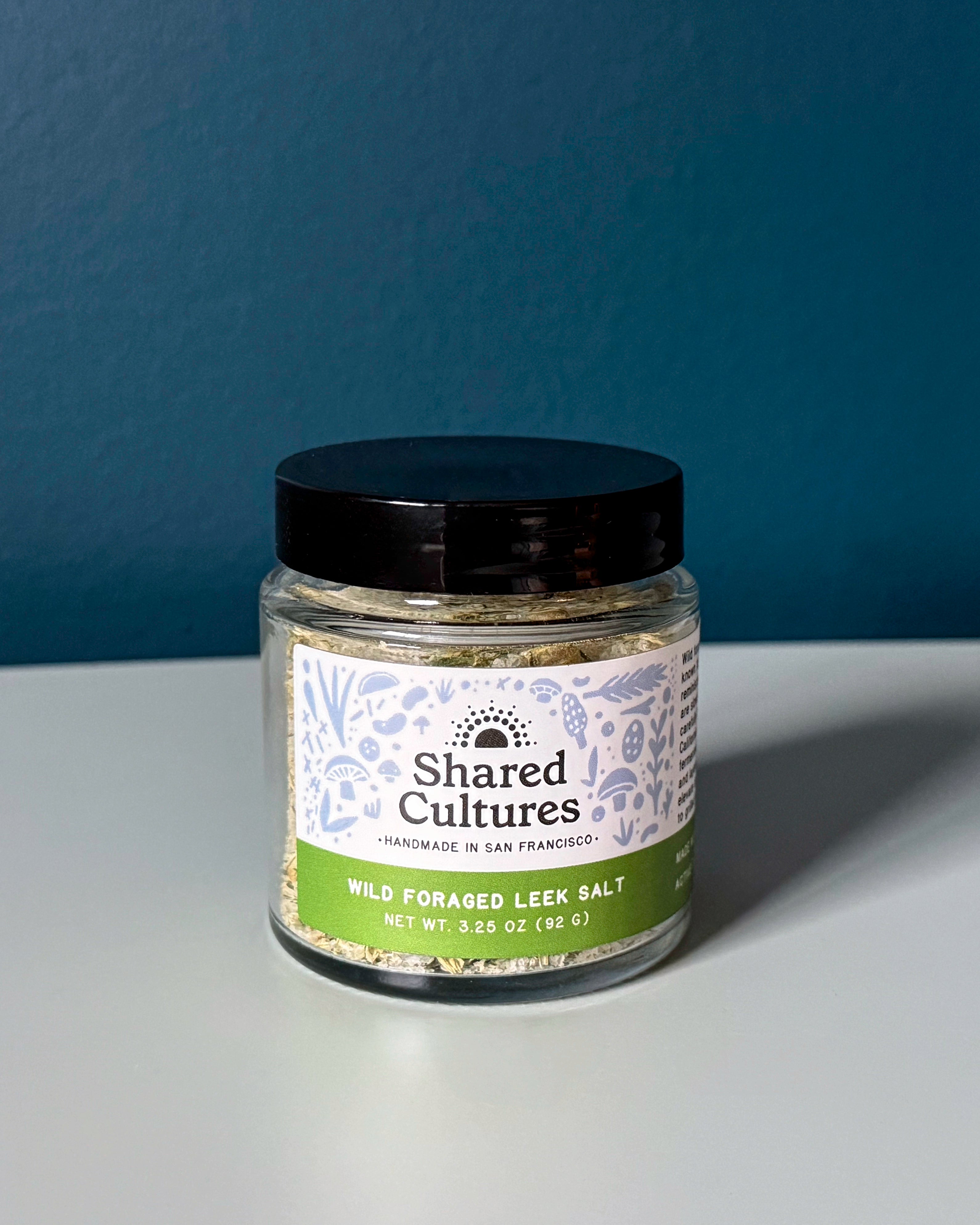 Jar of Shared Cultures wild foraged leek salt on a gray surface with a dark blue background